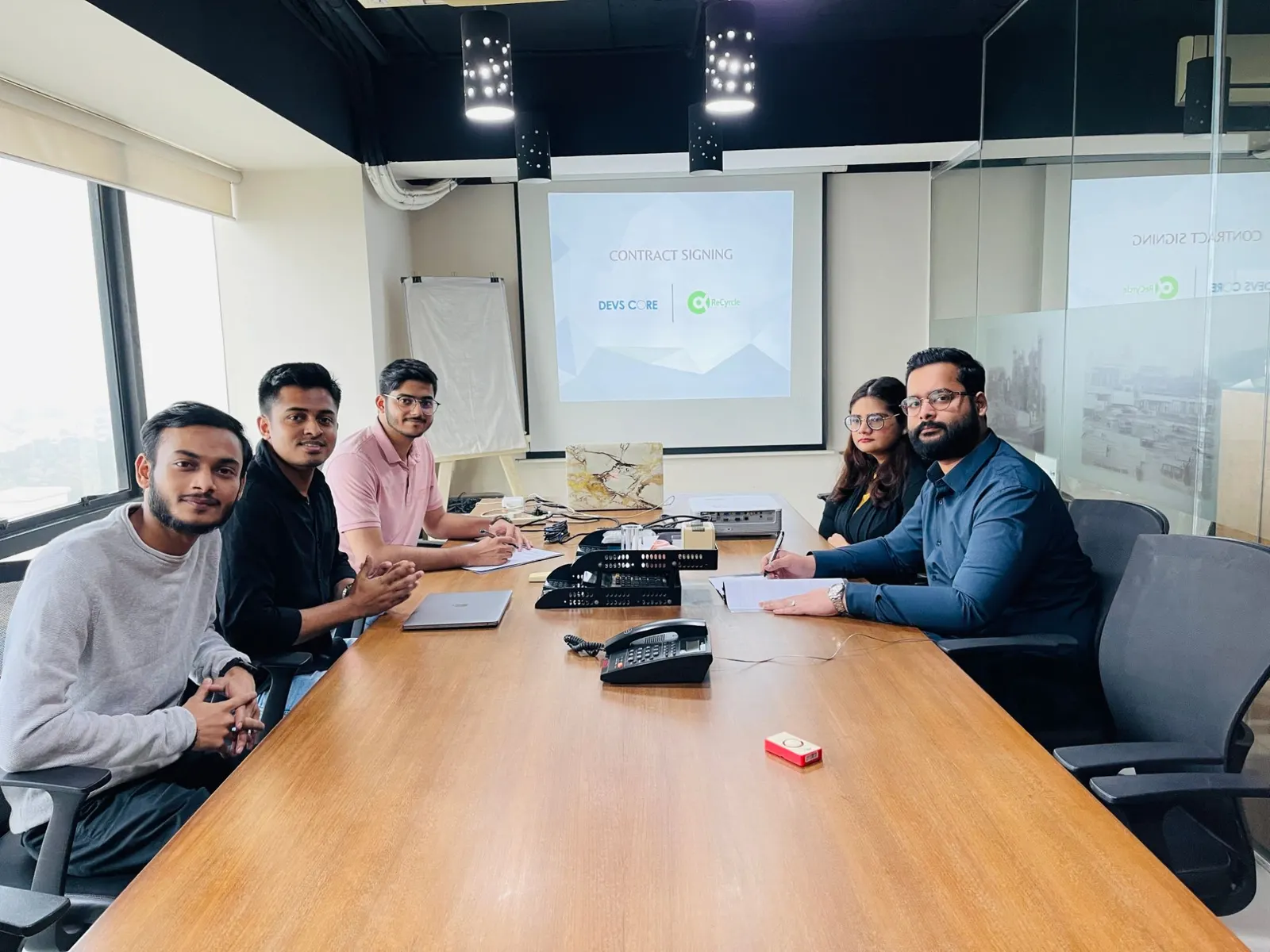 Devs Core and ReCyrcle teams at a meeting table signing a contract