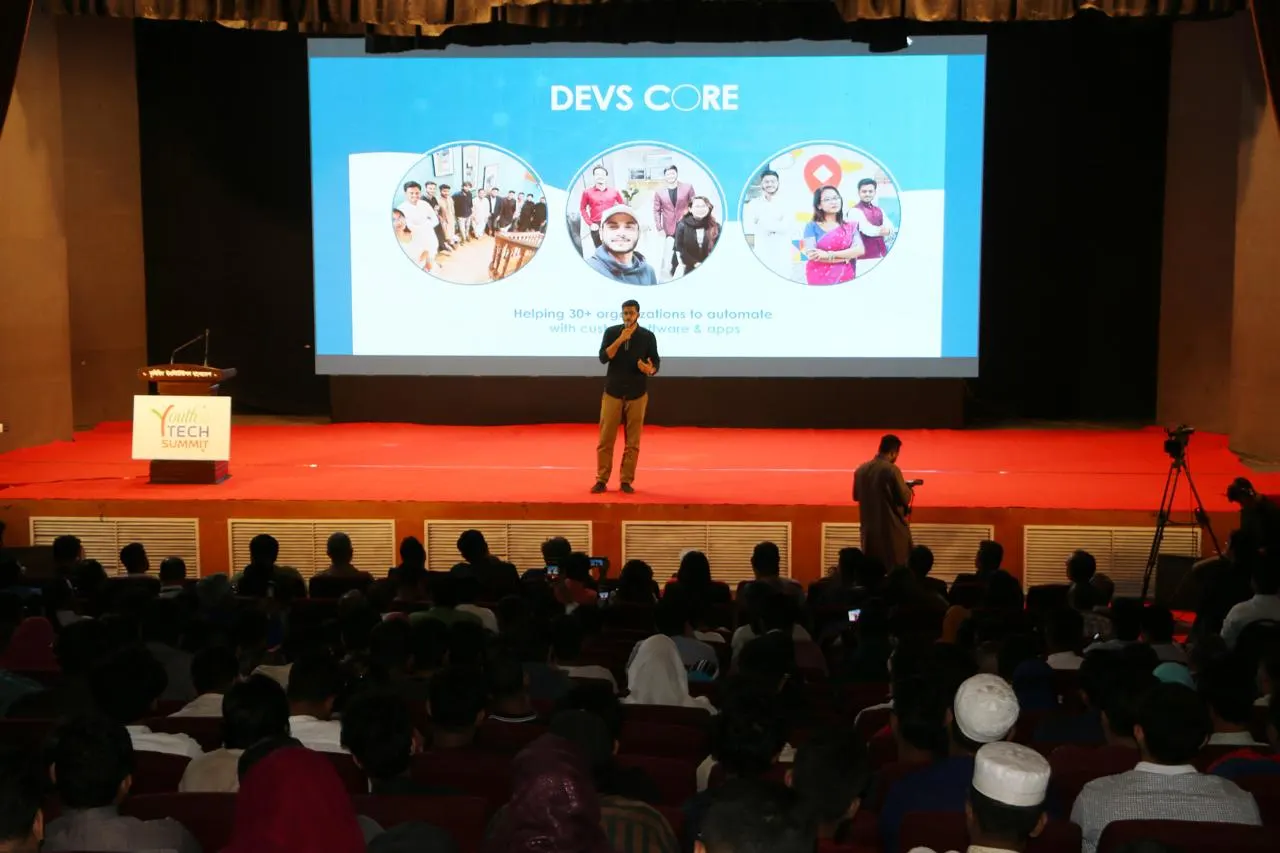 A talk on stage at Youth Tech Summit with Devs Core on the screen